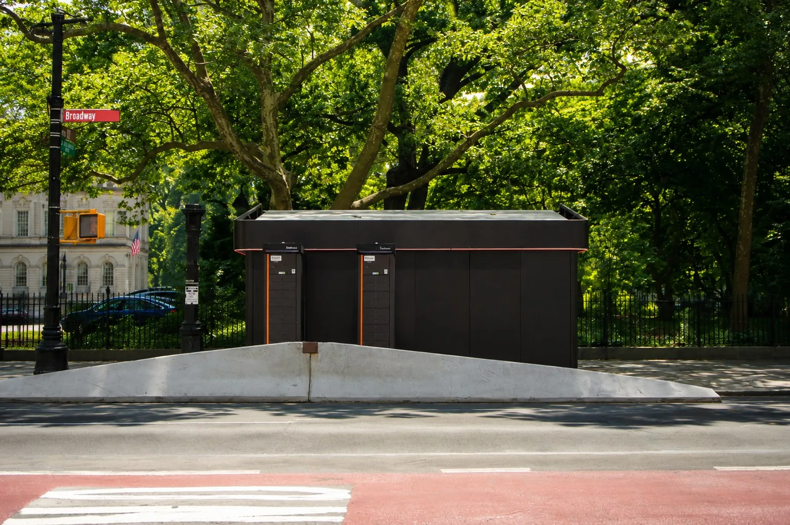 Two Swobbee Stations behind a low concrete kerb on Broadway in Lower Manhattan, with park trees behind them