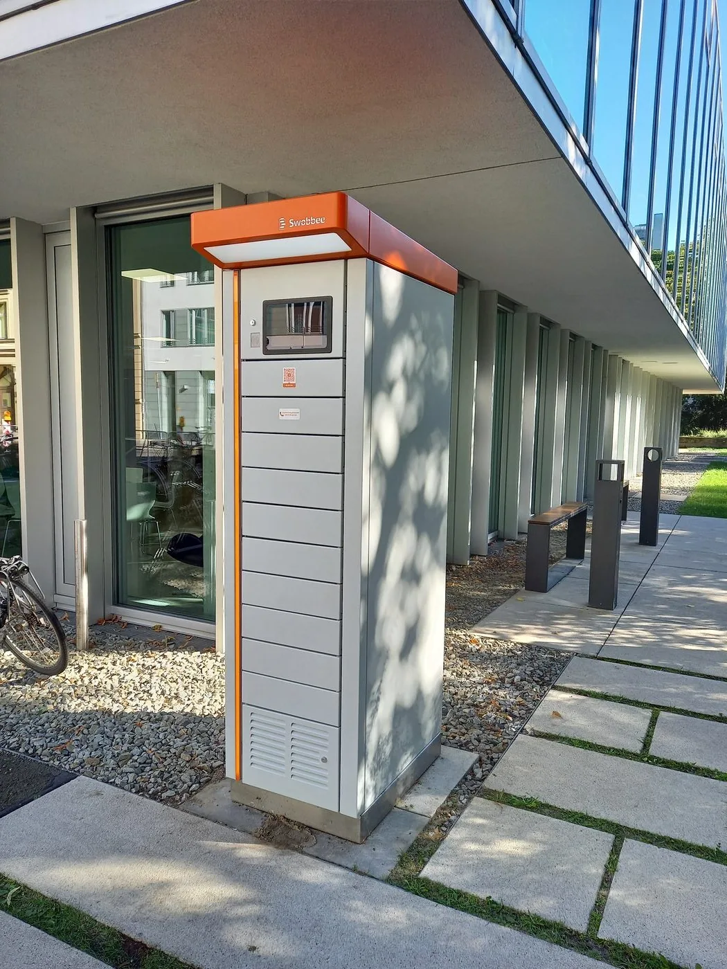 Eine grau-orange Swobbee Station auf einem gepflasterten Vorplatz neben einem Bürogebäude in Berlin