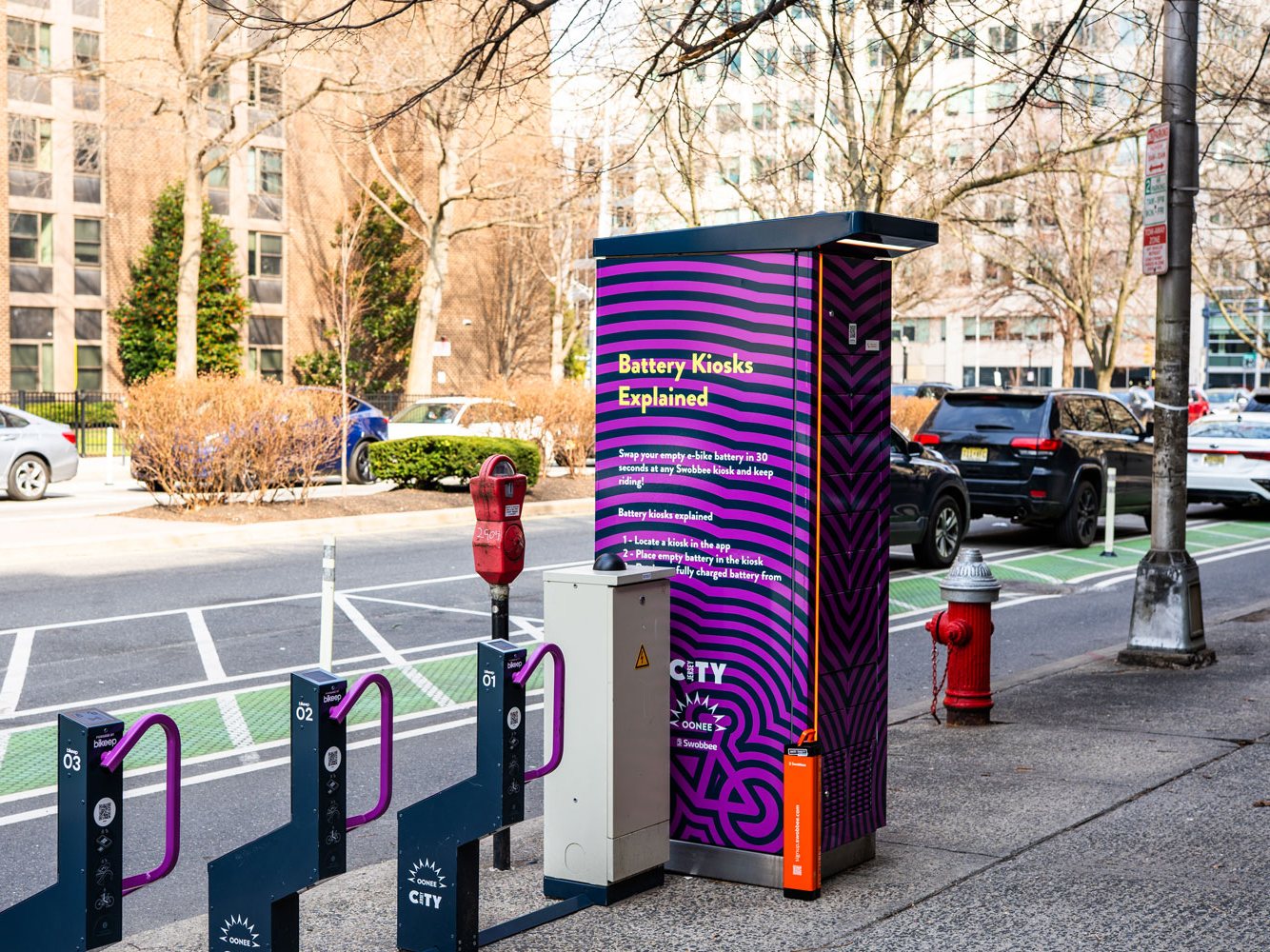 Ein Swobbee Akku-Kiosk auf einem Gehweg in Jersey City neben Fahrradständern
